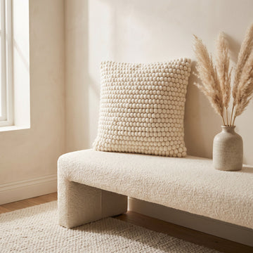 Natural ivory felted wool cushion on a cream boucle bench with a textured rug and dried pampas grass