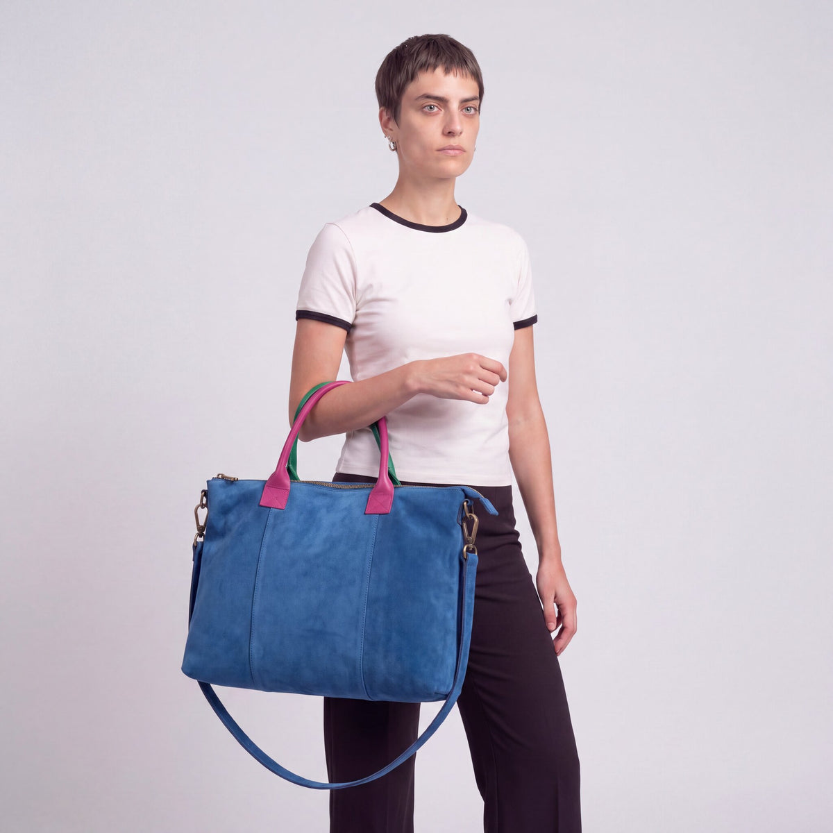 Model carrying the Blue Milano Max Suede Bag by both top handles, arm relaxed, studio shot