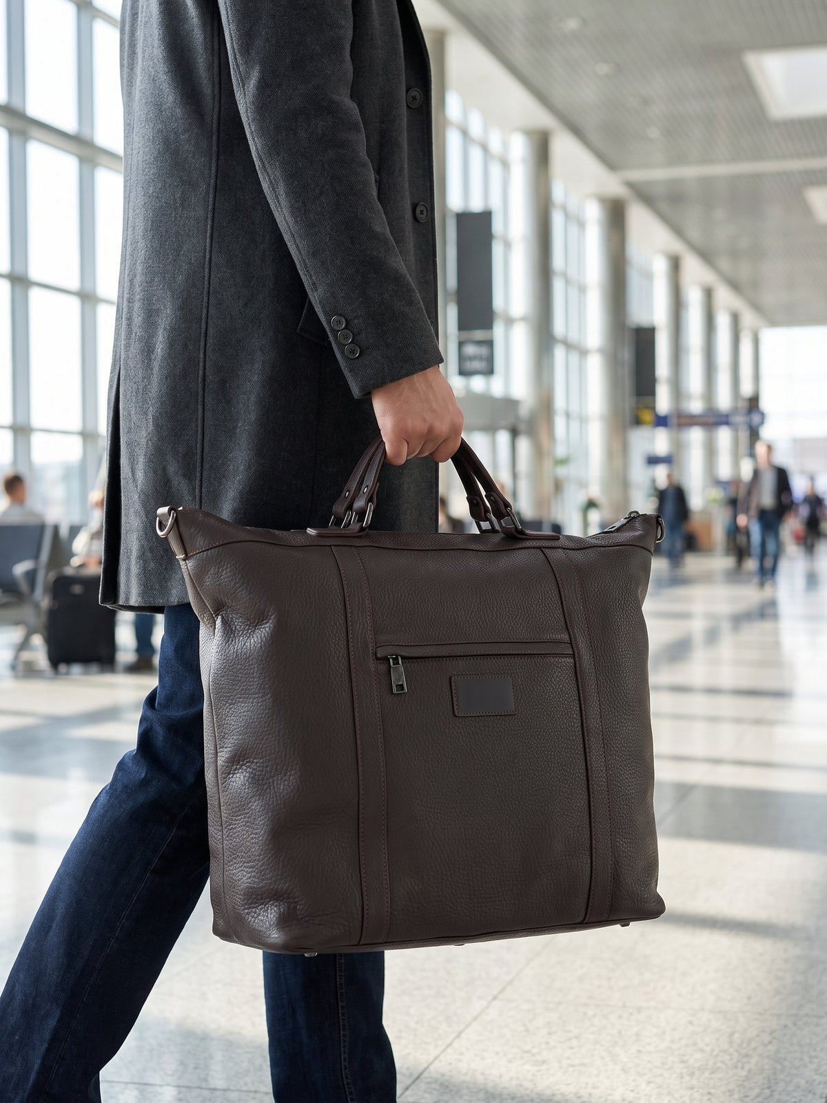 Man carrying the Alessio dark brown leather travel bag by Clemés through an airport terminal