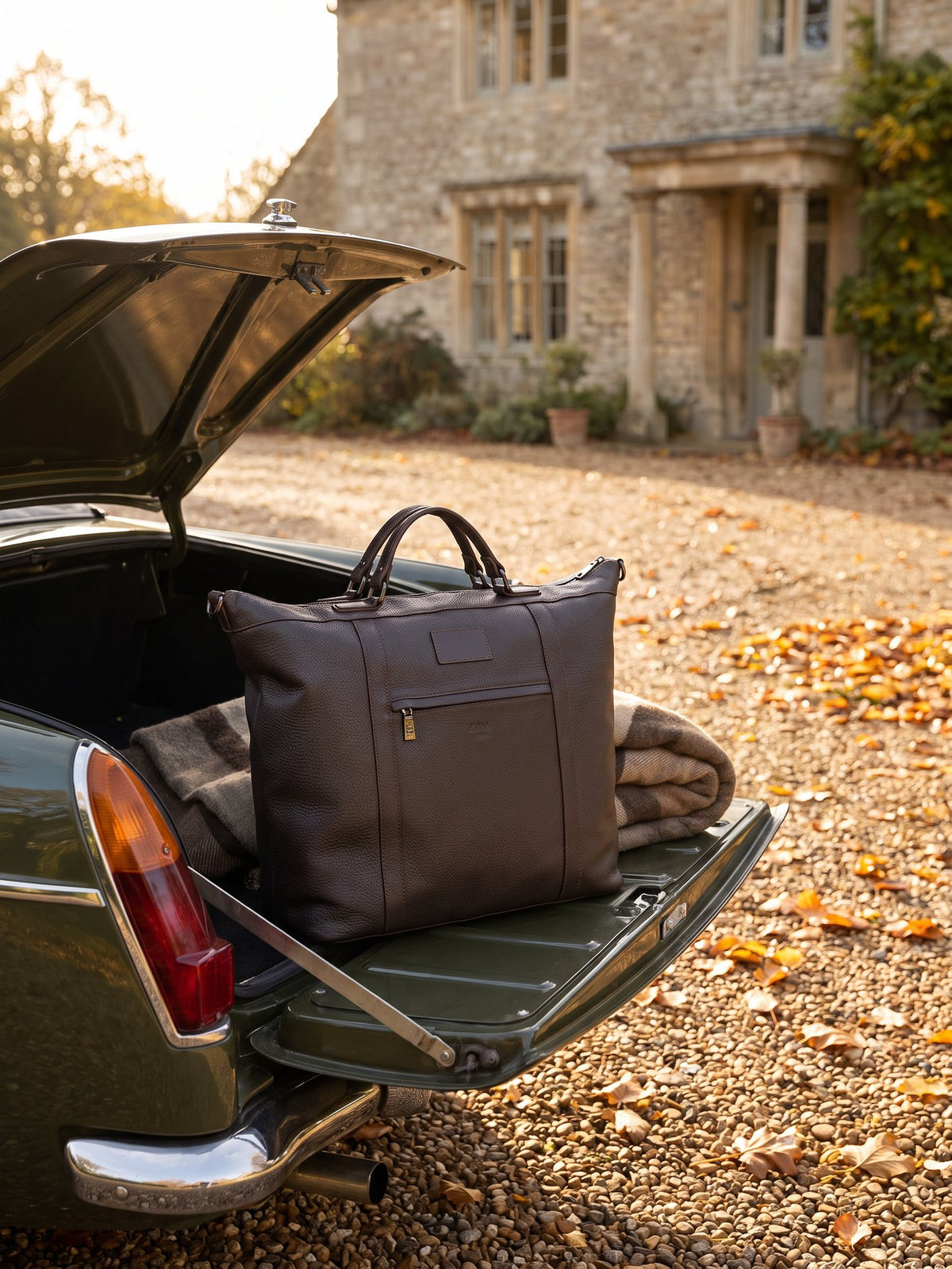 Alessio dark brown leather travel bag by Clemés in the open boot of a car on an autumn country drive