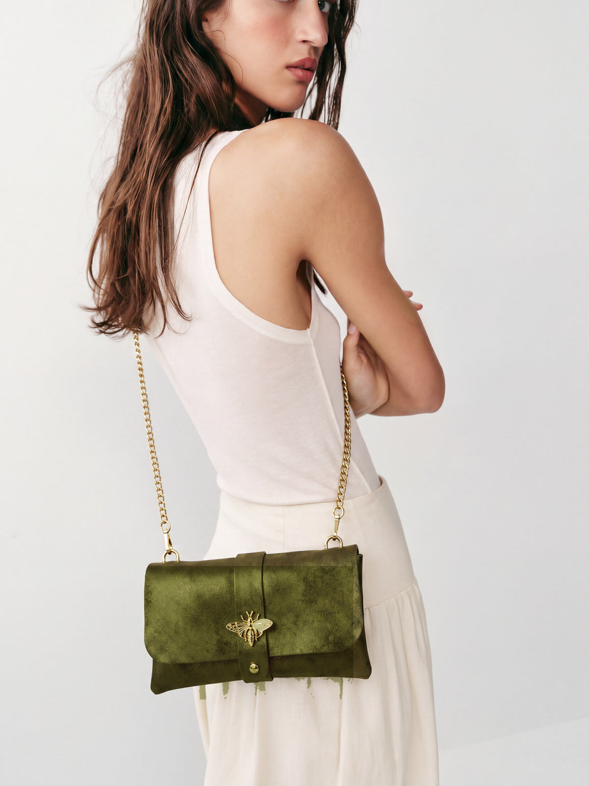 Model carrying the Olive Anima clutch crossbody on its gold chain, studio shot