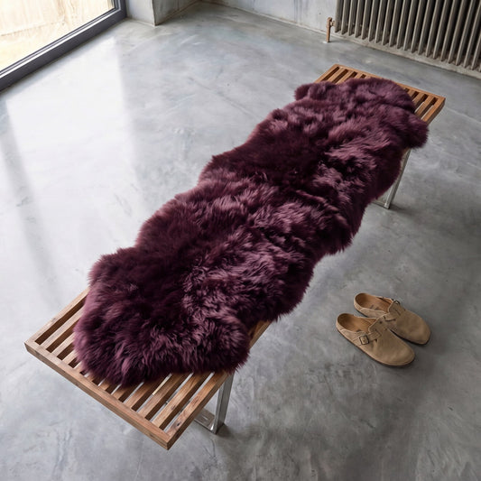 Aubergine double New Zealand sheepskin rug in deep plum laid along a wooden slatted bench on a concrete floor