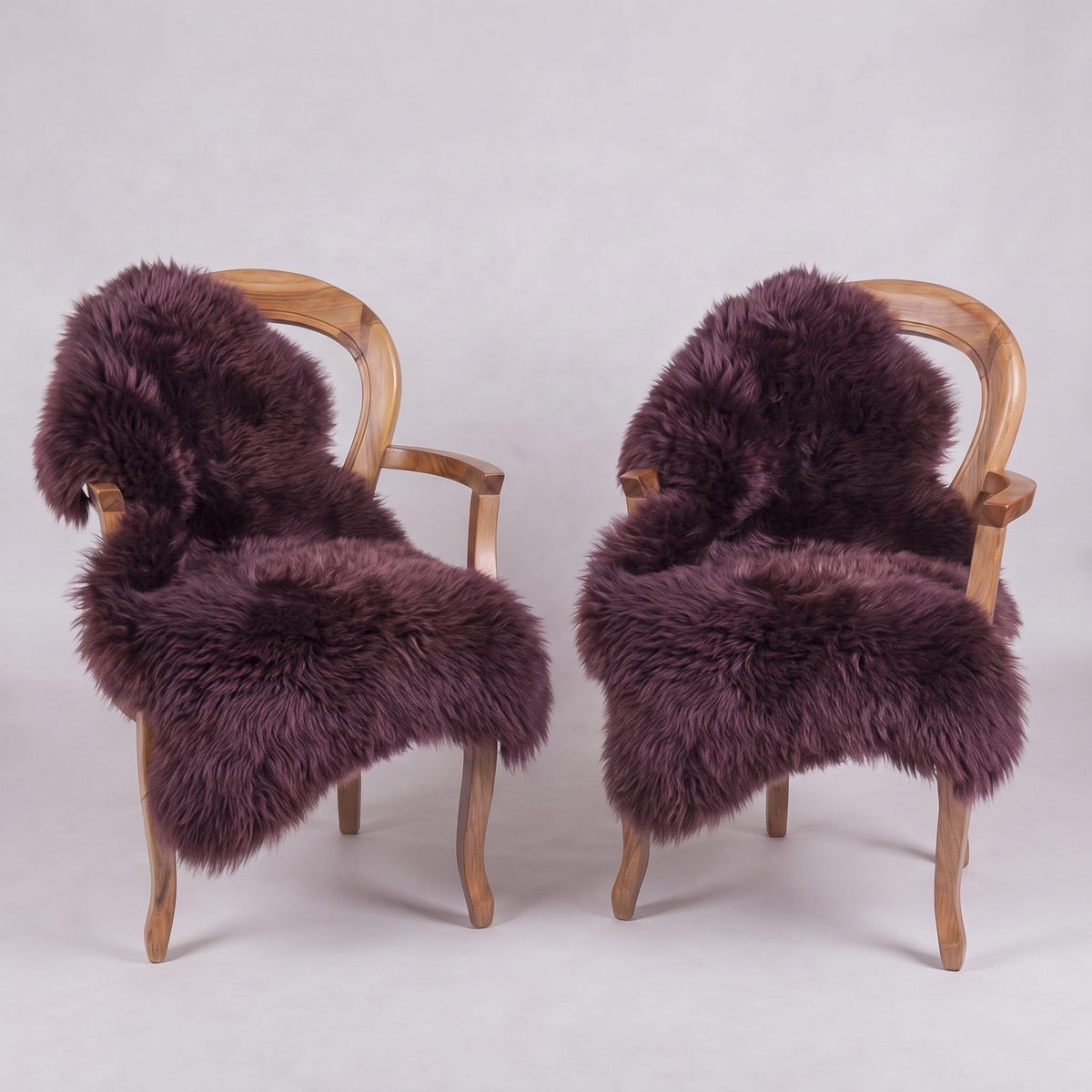 Pair of Aubergine New Zealand sheepskin throws, deep plum, draped over two wooden armchairs