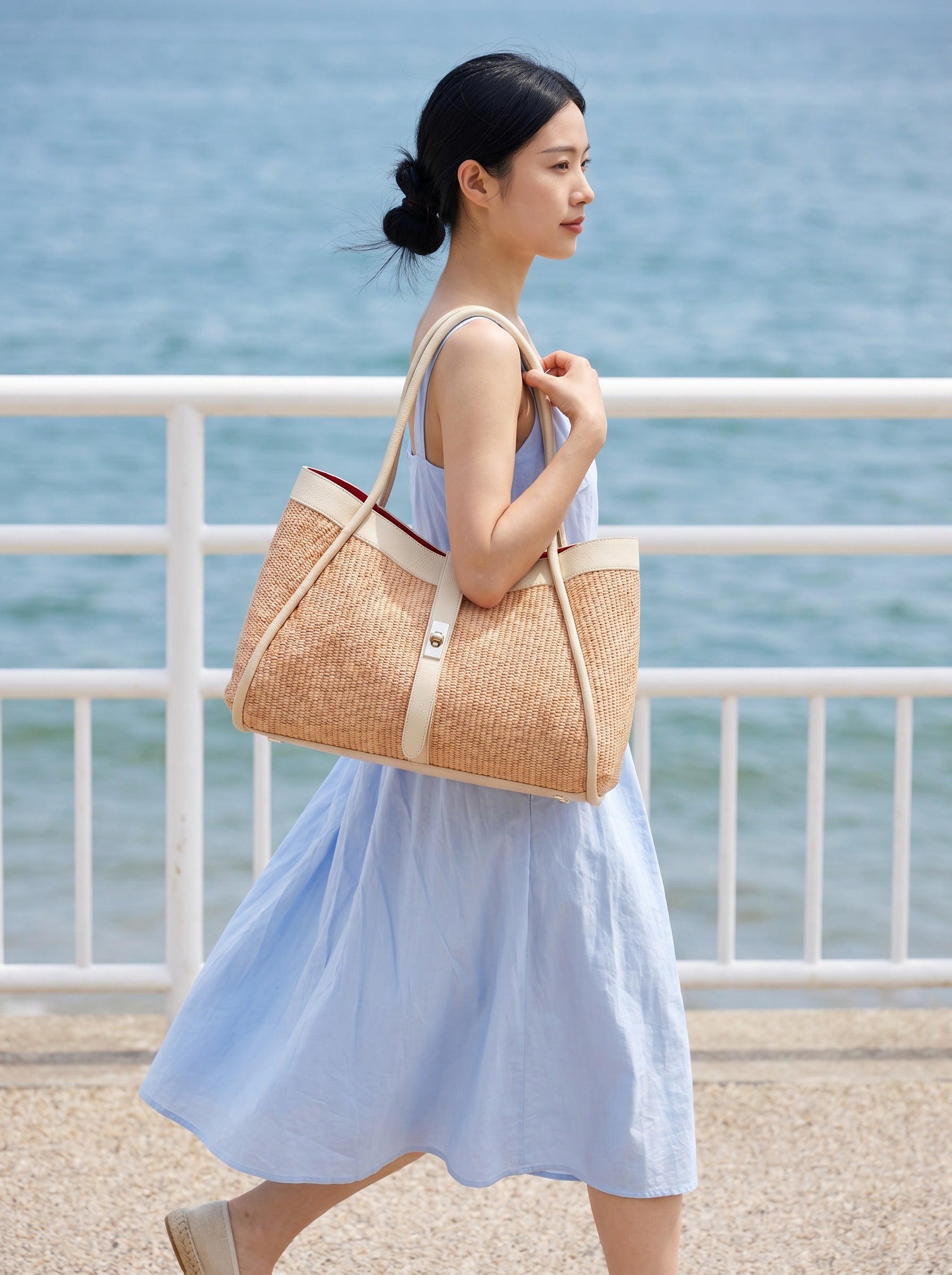 Woman carrying the Oyster Bianca Large Raffia Handbag along a seaside promenade