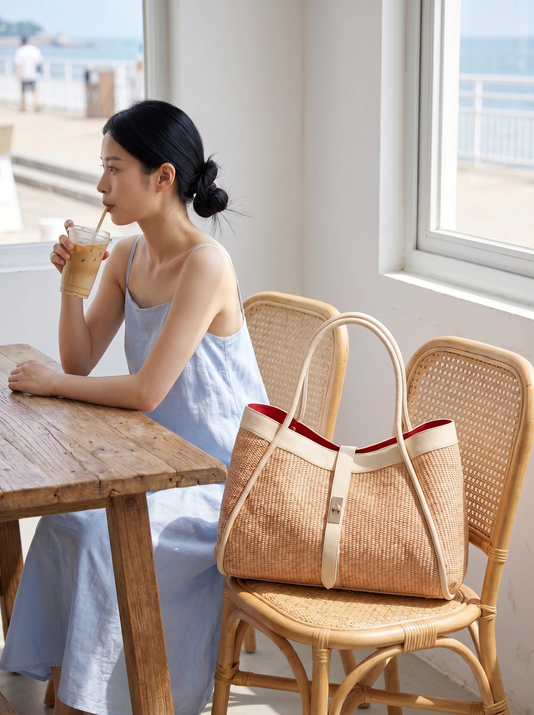 Oyster Bianca Large Raffia Handbag on a rattan chair at a bright coastal café