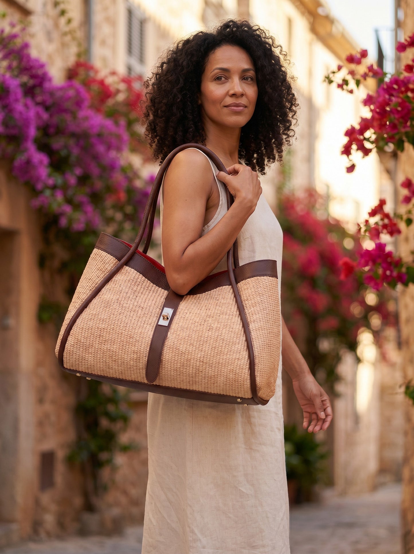 Woman carrying the Dark Brown Bianca Large Raffia Handbag in an old-town street with bougainvillea