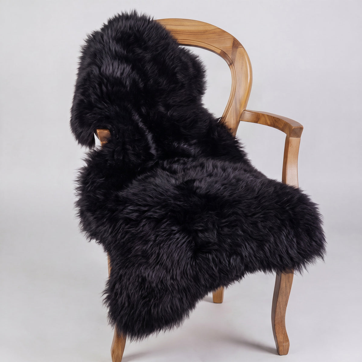Black single long wool sheepskin rug draped over a wooden armchair