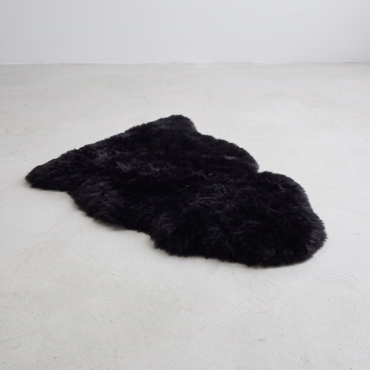 Black single sheepskin rug flat on a pale grey floor
