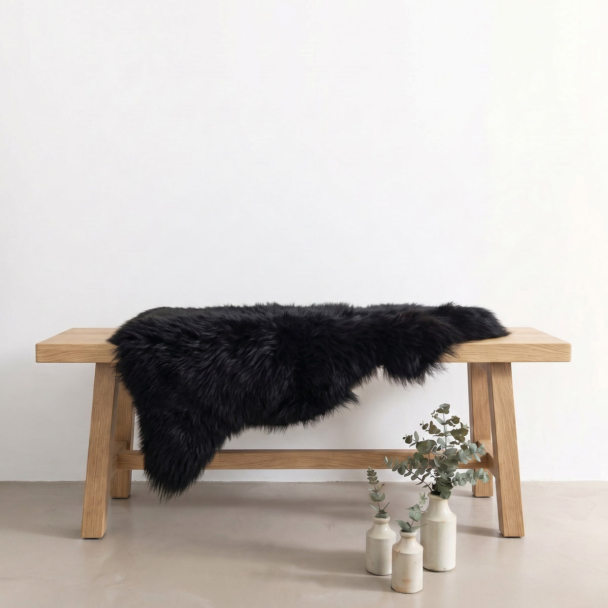 Black sheepskin rug draped over an oak bench