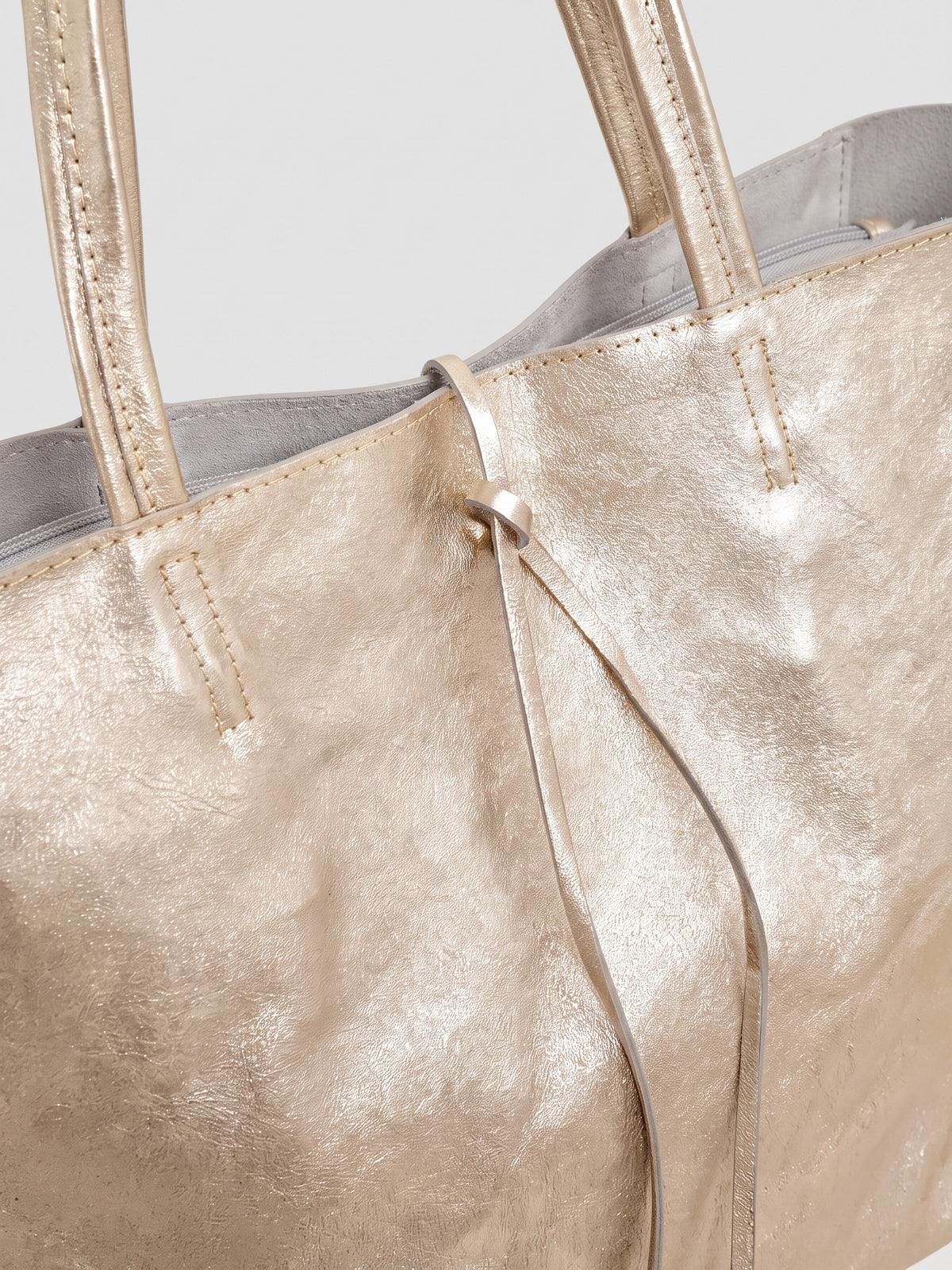 Carlotta oversized leather tote by Clemés in Champagne Gold metallic leather, close-up of the top edge with rolled handles and knotted leather tie