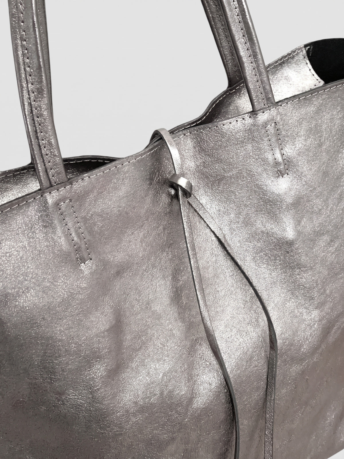 Carlotta oversized leather tote by Clemés in Titanium metallic leather, close-up of the top edge with rolled handles and knotted leather tie