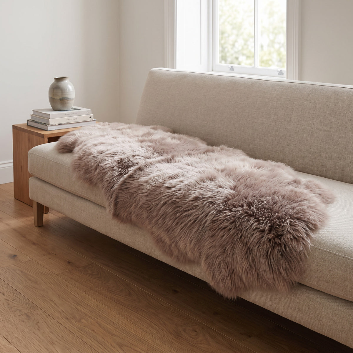 Taupe double sheepskin throw draped over a linen sofa in a light Scandinavian living room