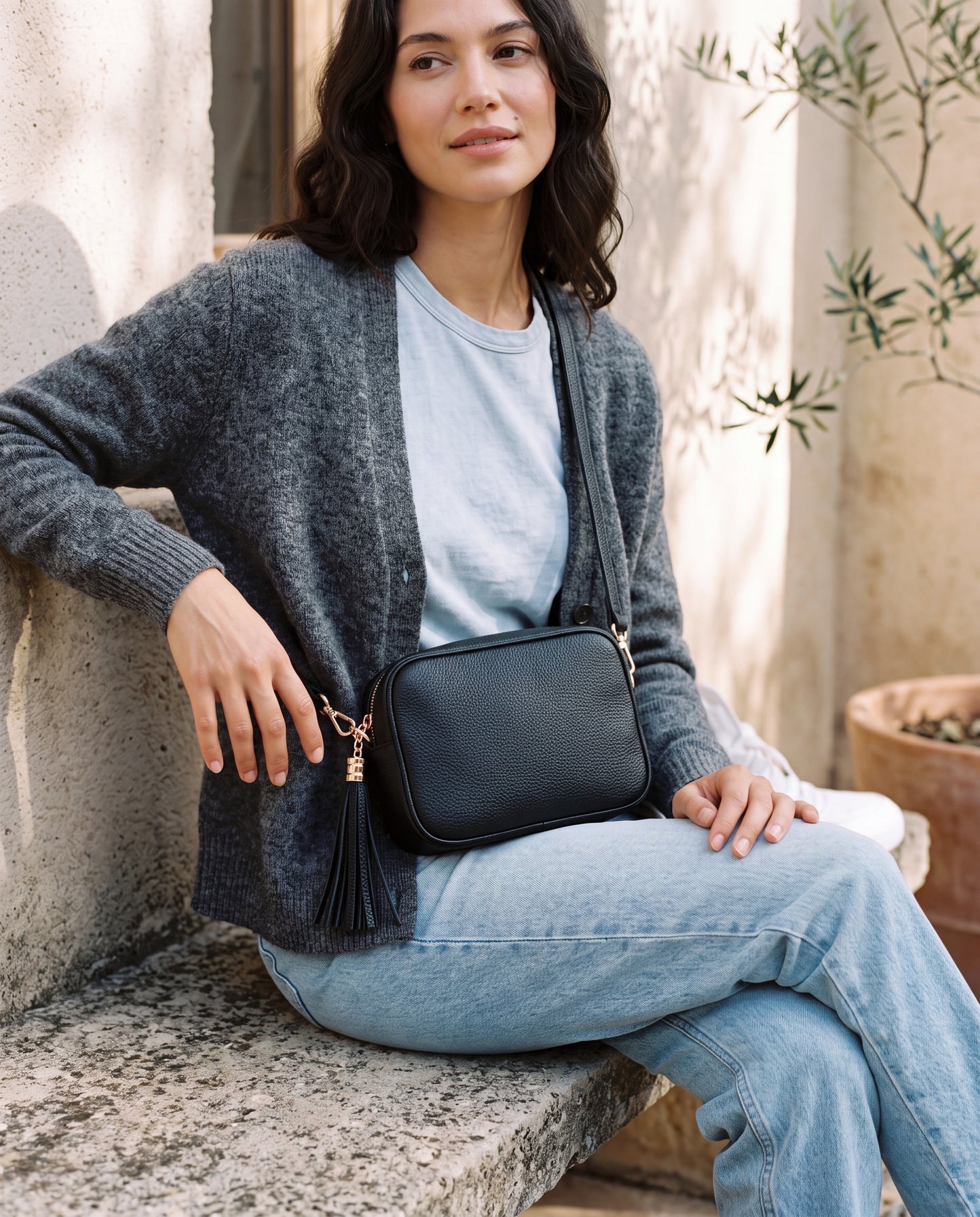 Model with the Black Éloise Leather Tassel Camera Bag by Clemés on a sunny courtyard bench