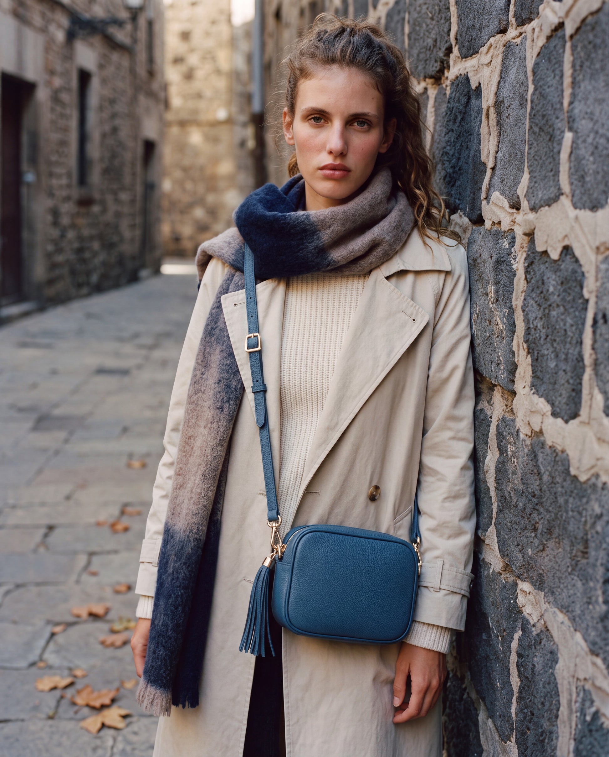 Model with the Navy Éloise Leather Tassel Camera Bag by Clemés on a stone-walled street with a scarf