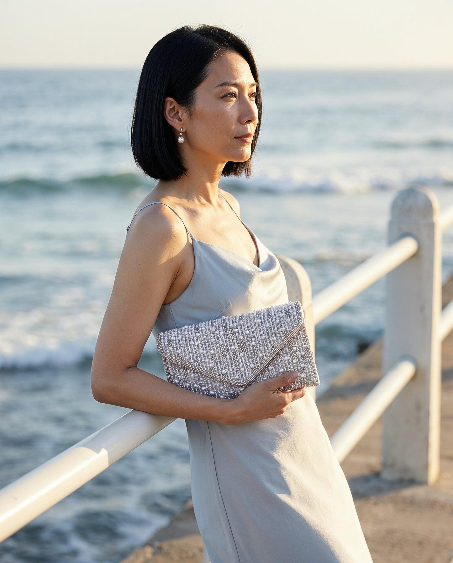Woman with the Silver Perlette Pearl & Crystal Envelope Clutch on a seaside promenade at golden hour