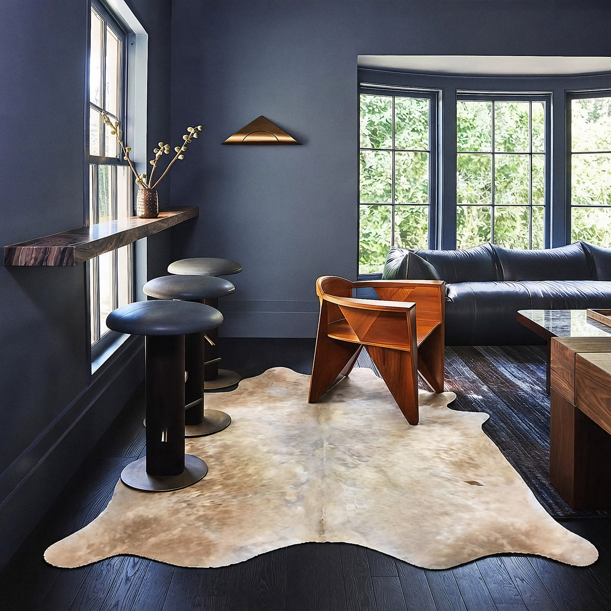 Tan and white cowhide rug styled on the floor of a moody dark blue living room