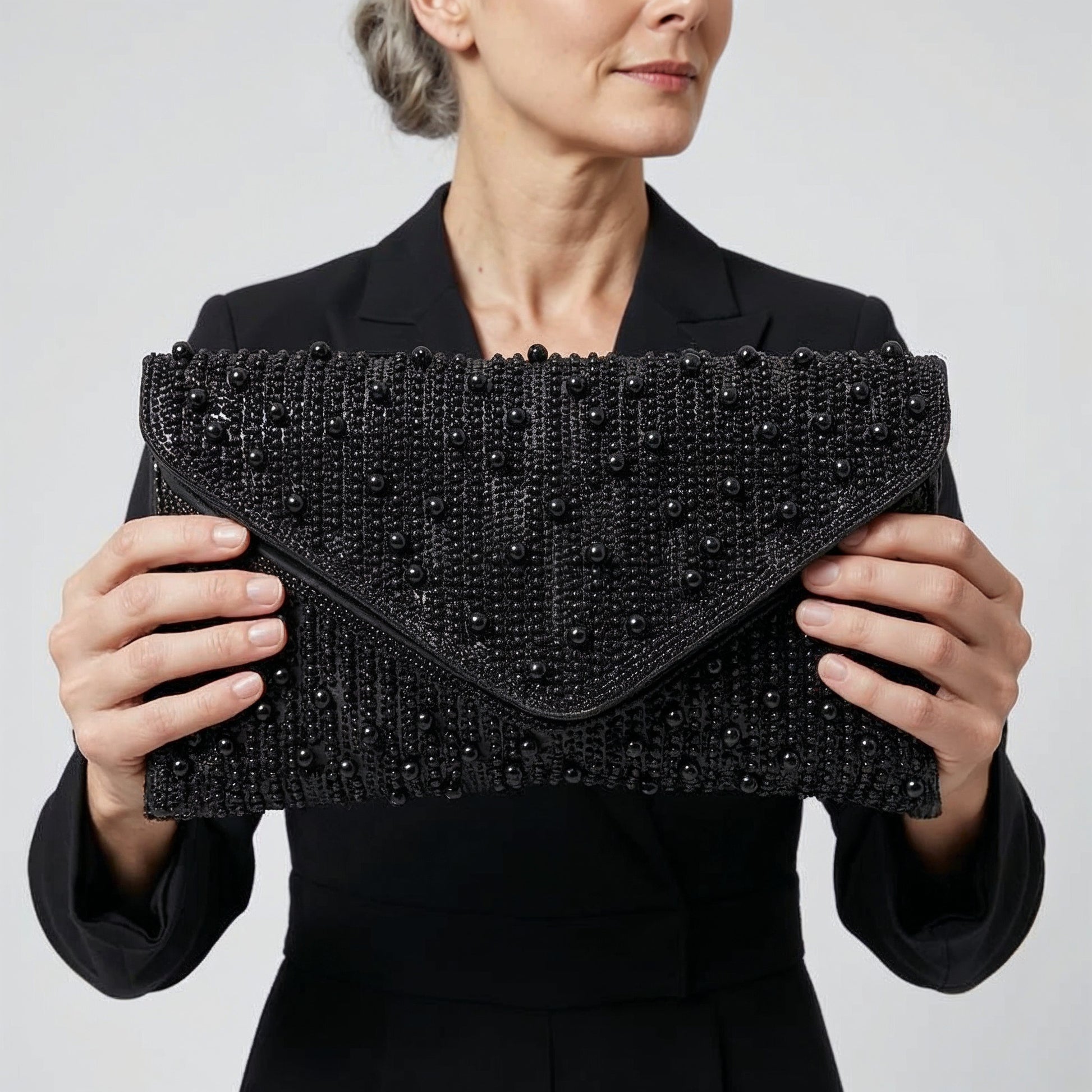 Model presenting the Black Perlette Pearl & Crystal Envelope Clutch to the camera, studio hero shot
