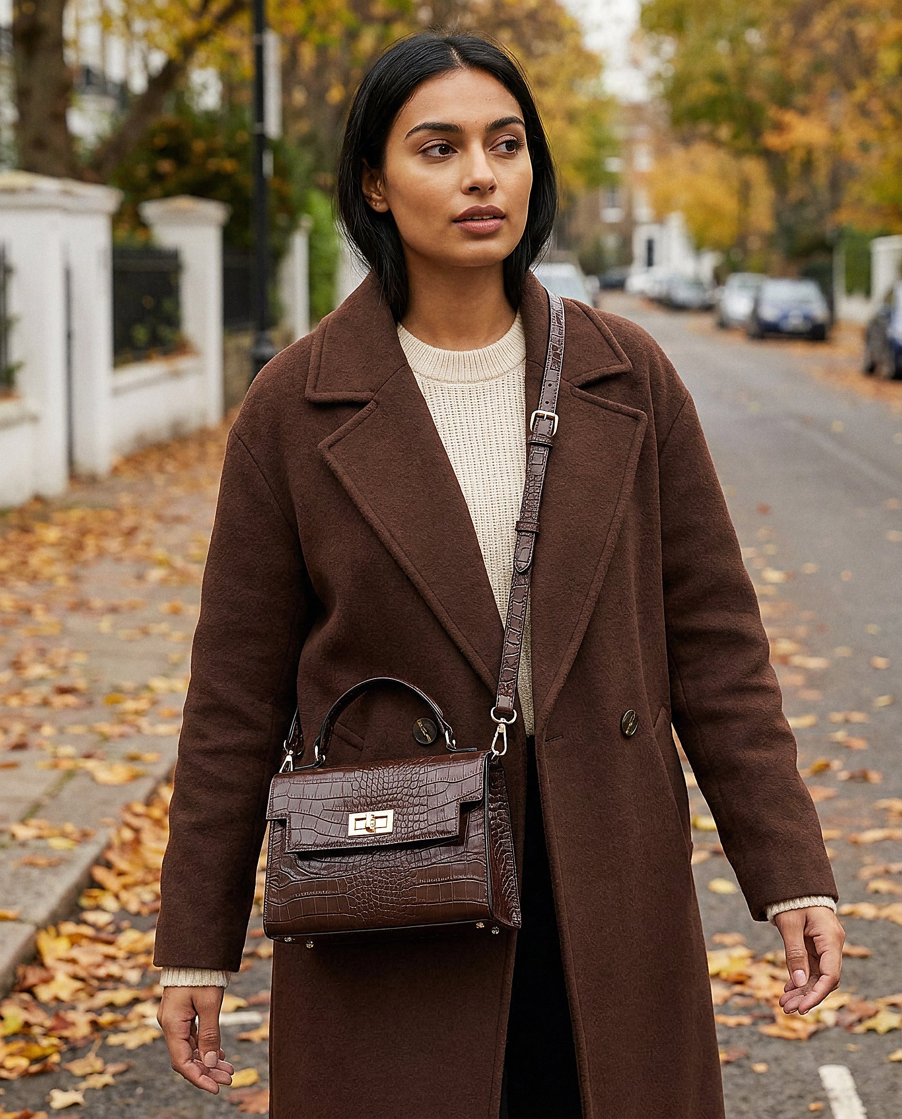 Woman with the Chocolate Margot Croc crossbody bag on an autumn street with fallen leaves