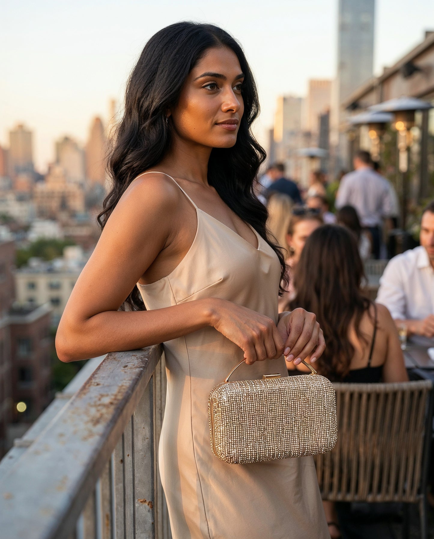 Woman with the Gold Odette Crystal Minaudière Clutch at a golden-hour rooftop bar