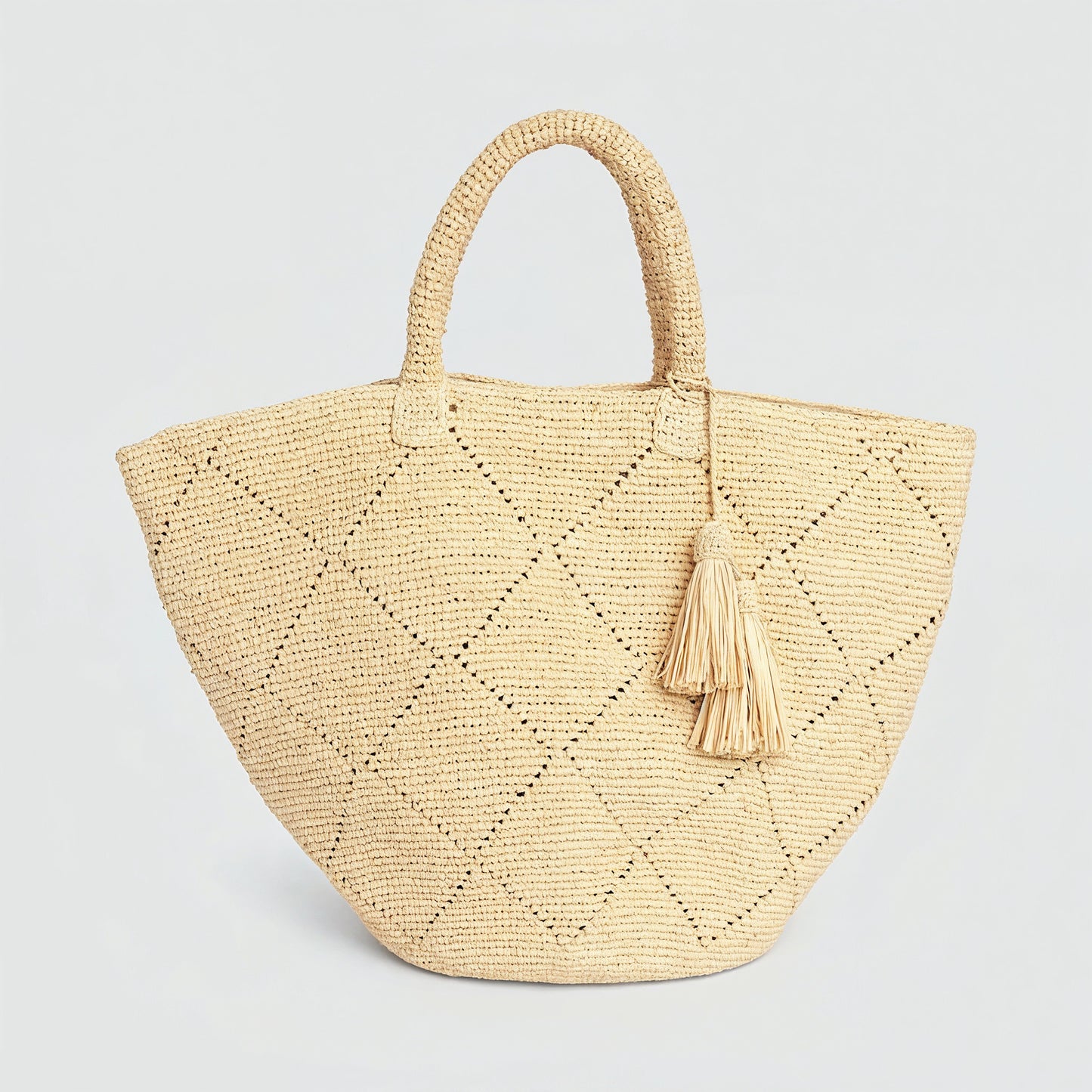 Amandine natural raffia basket tote with leather tassel on a light grey studio background