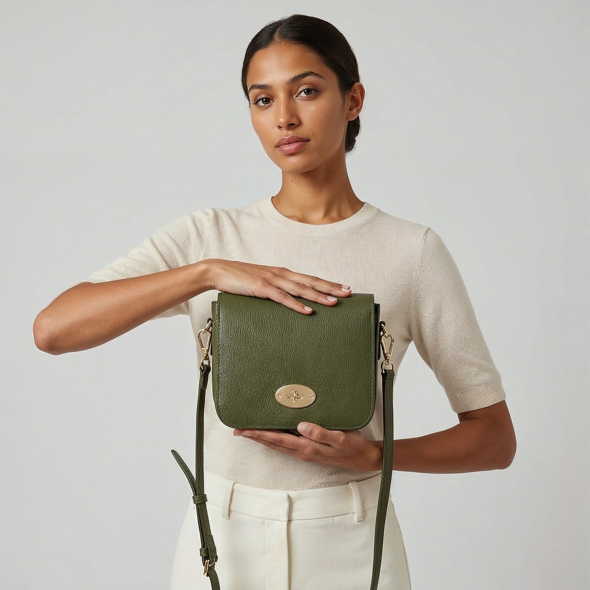 Close-up of the Dark Olive Chiara crossbody bag and gold turn-lock clasp held in both hands