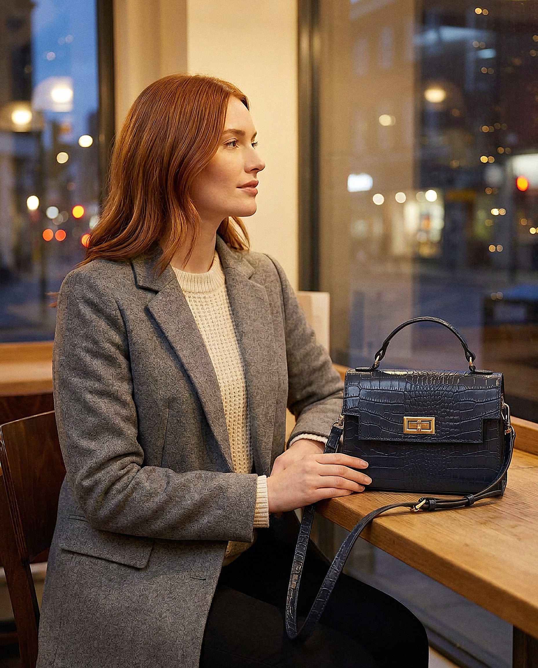 Woman with the Navy Margot Croc crossbody bag at a cosy café in the evening