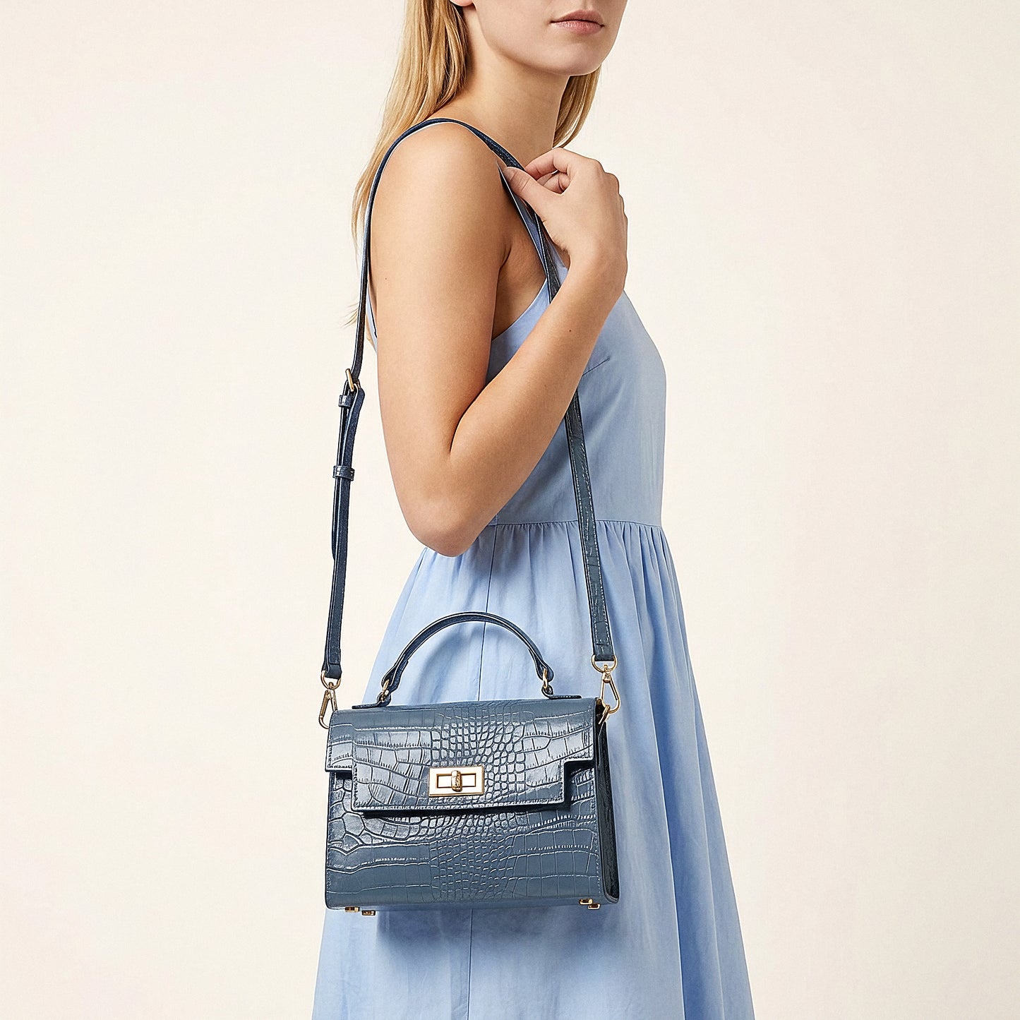 Model carrying the Dusty Blue Margot Croc crossbody bag on her shoulder, studio shot