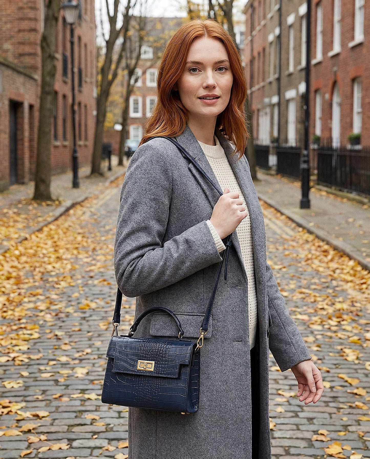 Woman with the Navy Margot Croc crossbody bag on an autumn city street with fallen leaves