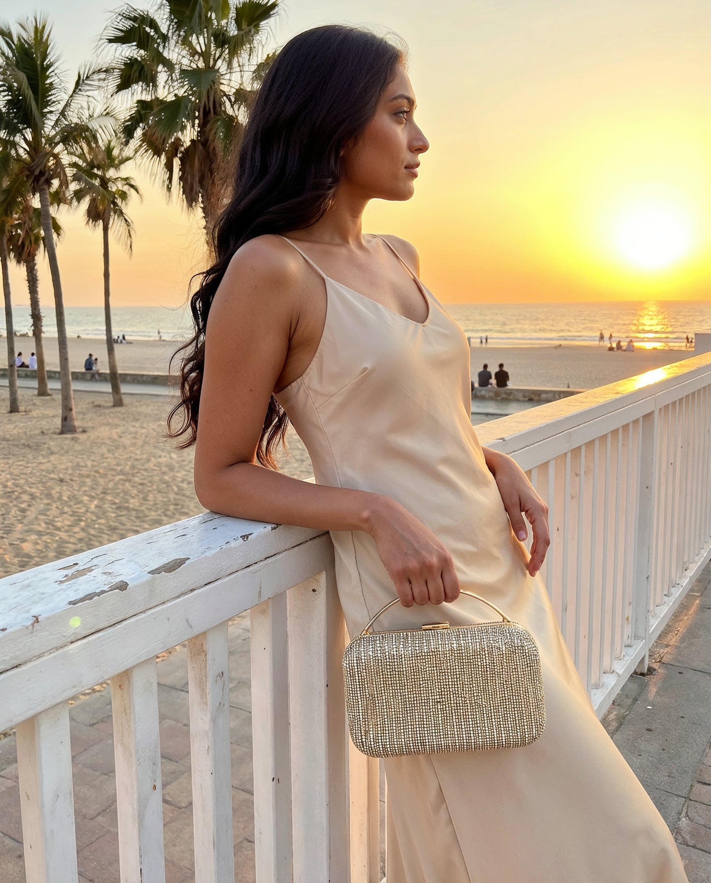 Woman with the Gold Odette Crystal Minaudière Clutch on a seaside promenade at sunset