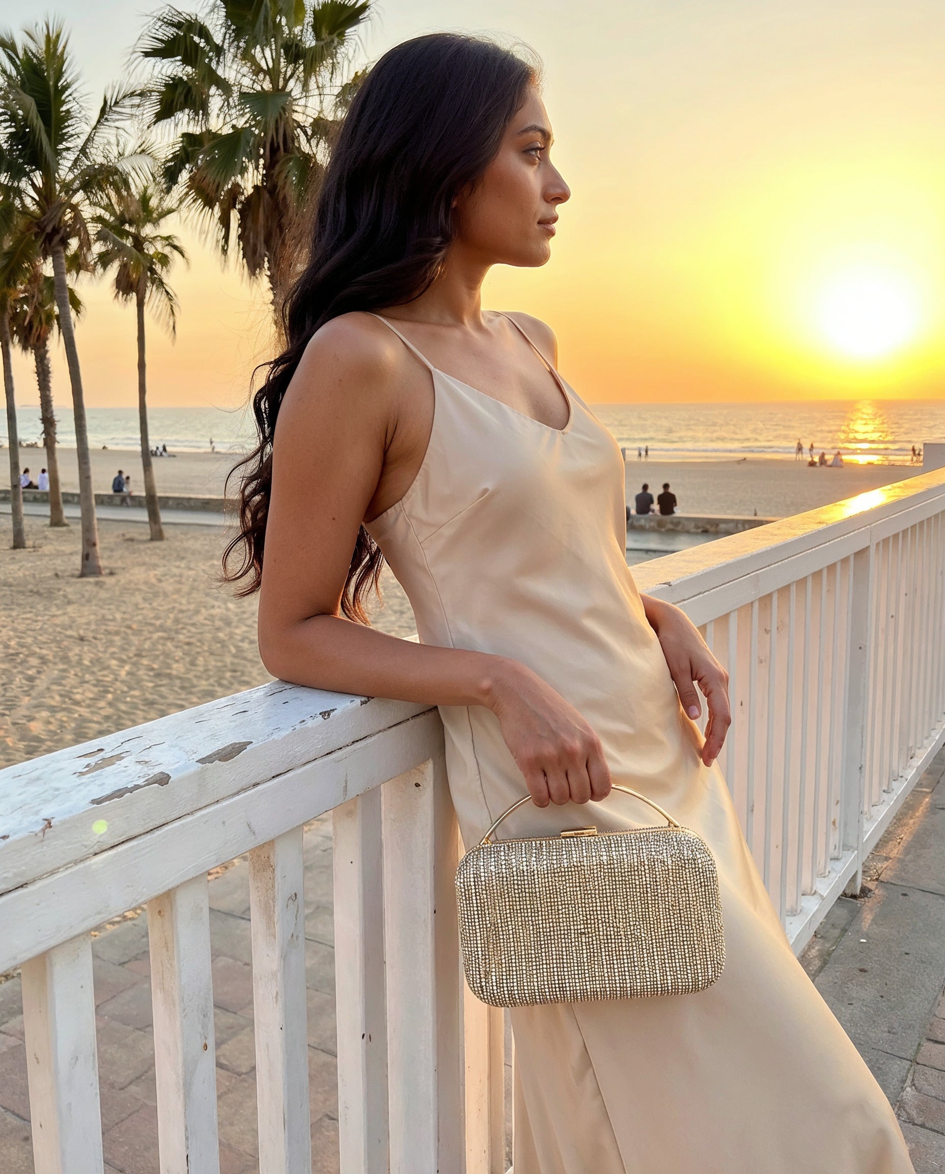 Woman with the Gold Odette Crystal Minaudière Clutch on a seaside promenade at sunset