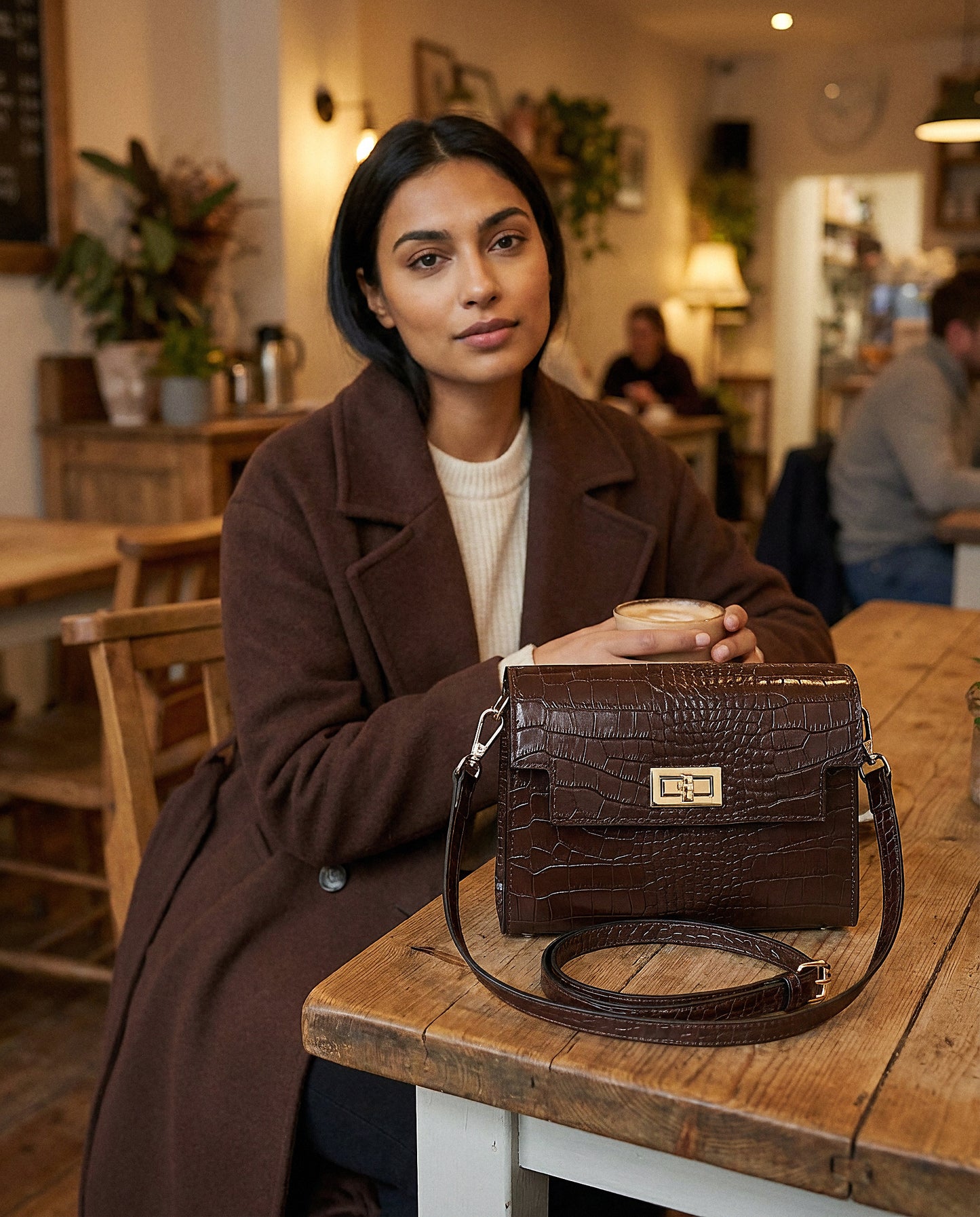 Woman with the Chocolate Margot Croc crossbody bag in a cosy café interior