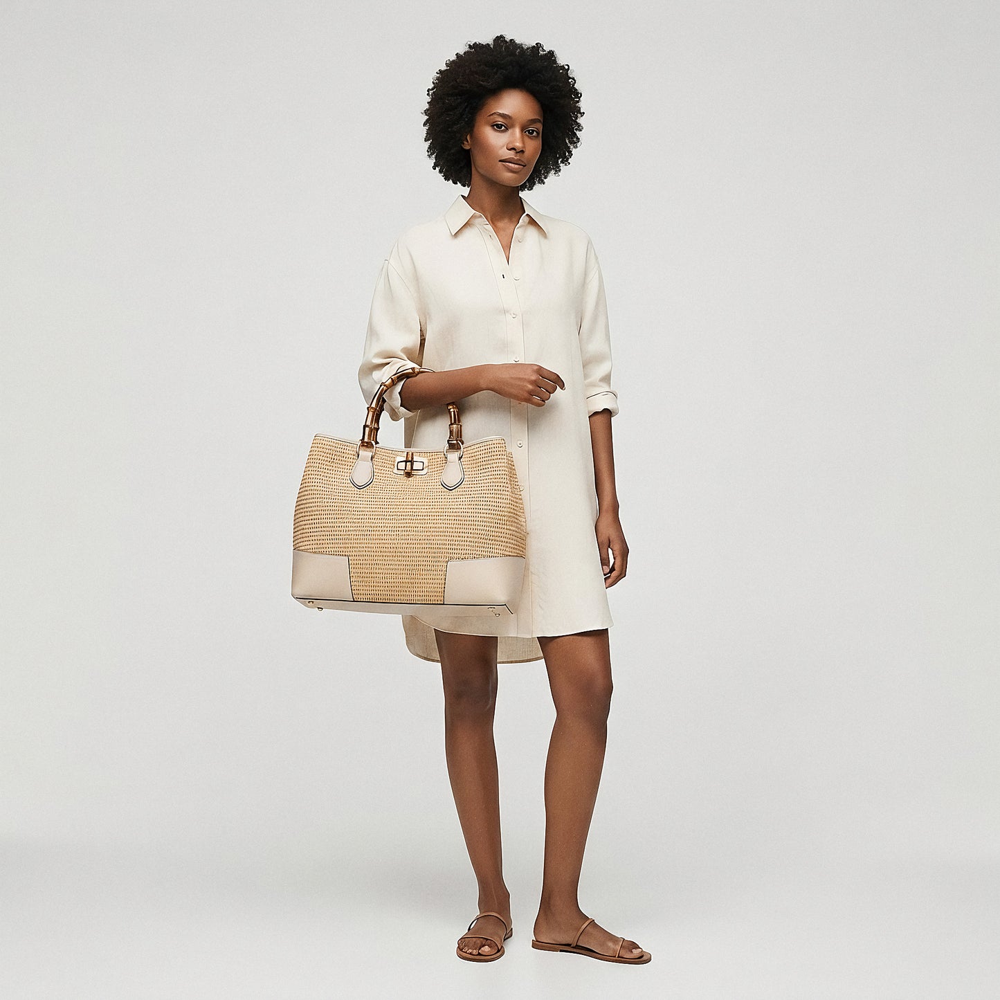 Model holding the Oyster Ginevra Bamboo-Handle Raffia Bag by Clemés by its top handle, studio shot