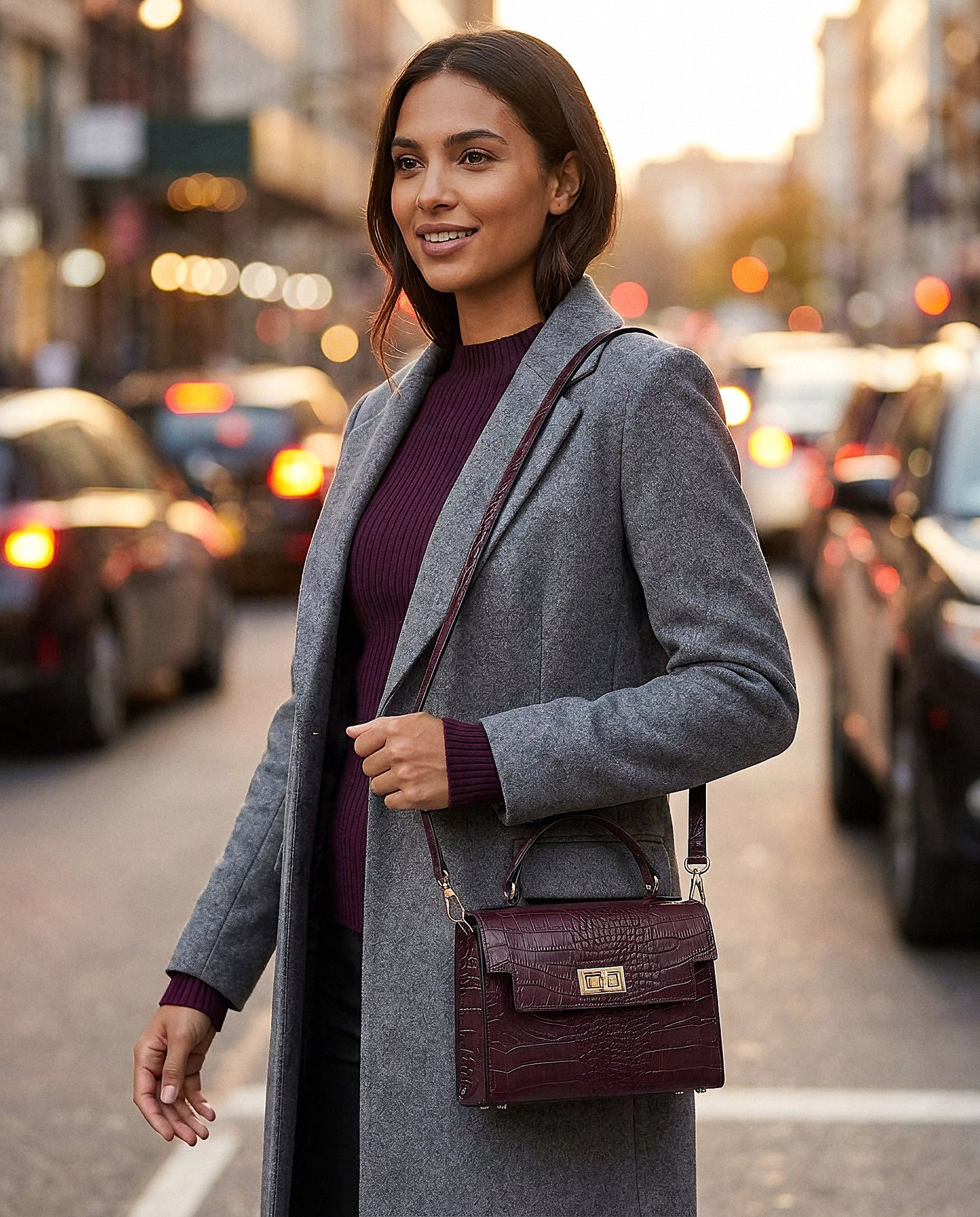 Woman with the Aubergine Margot Croc crossbody bag on an evening city street with lights