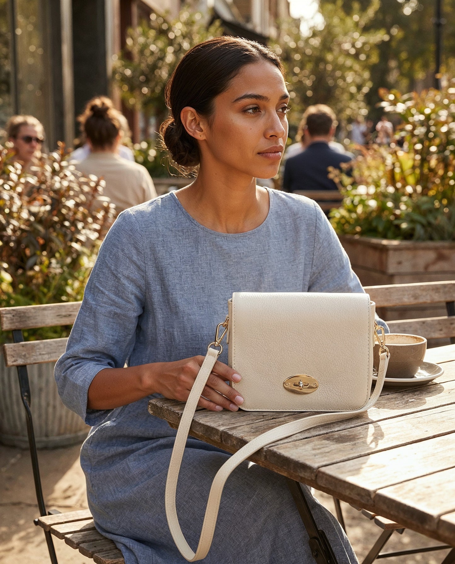 Woman with the Oyster Chiara crossbody bag at a sunny cafe terrace