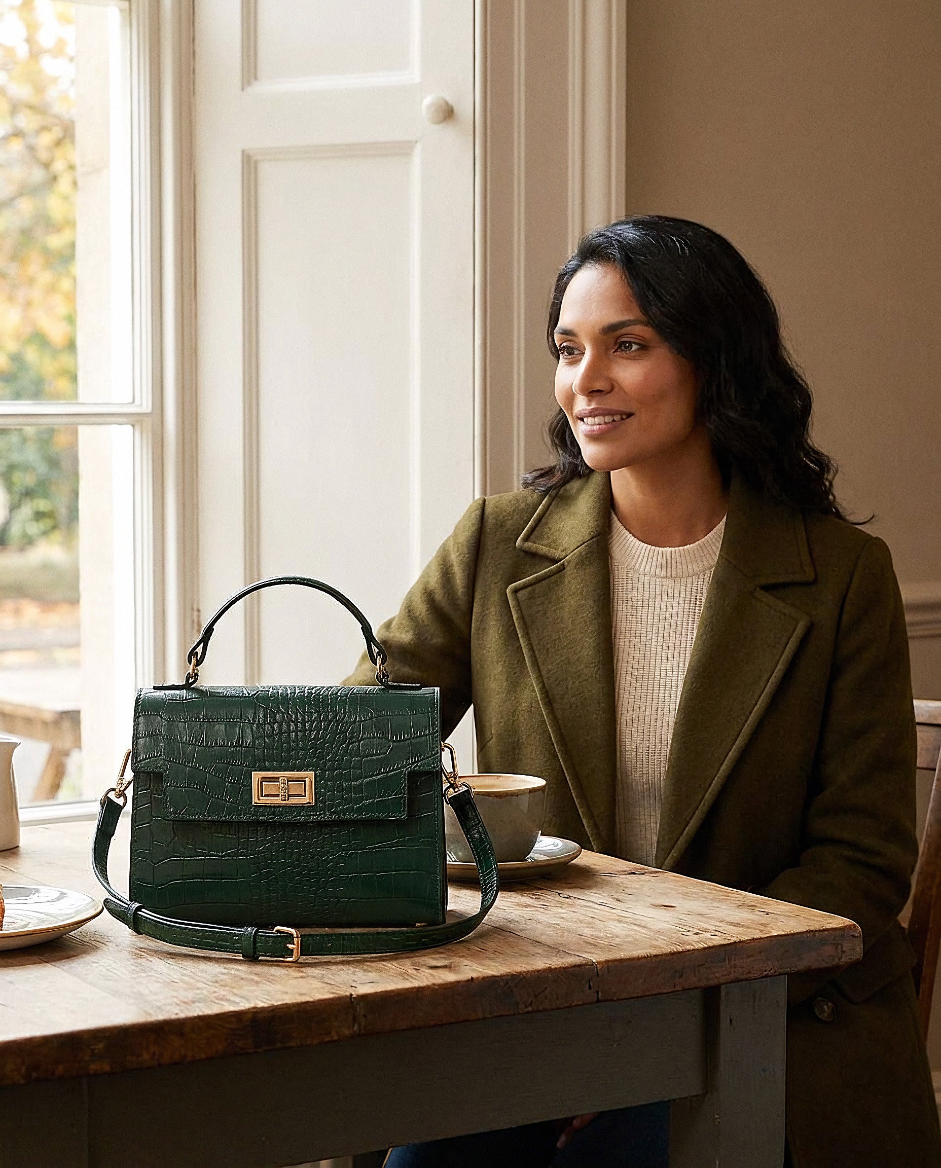 Woman with the Forest Green Margot Croc crossbody bag in a cosy café interior
