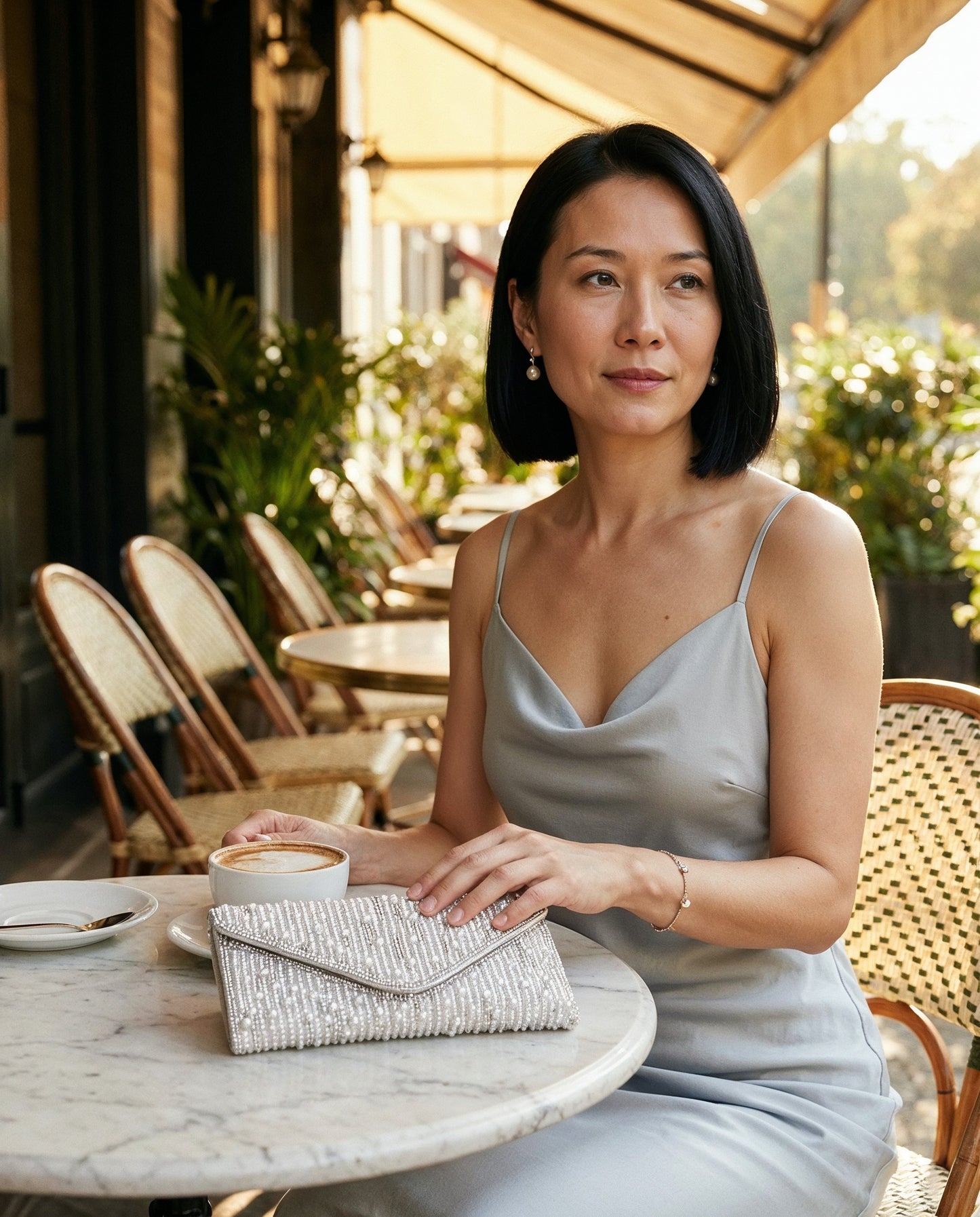 Woman with the Silver Perlette Pearl & Crystal Envelope Clutch at a sunlit café terrace