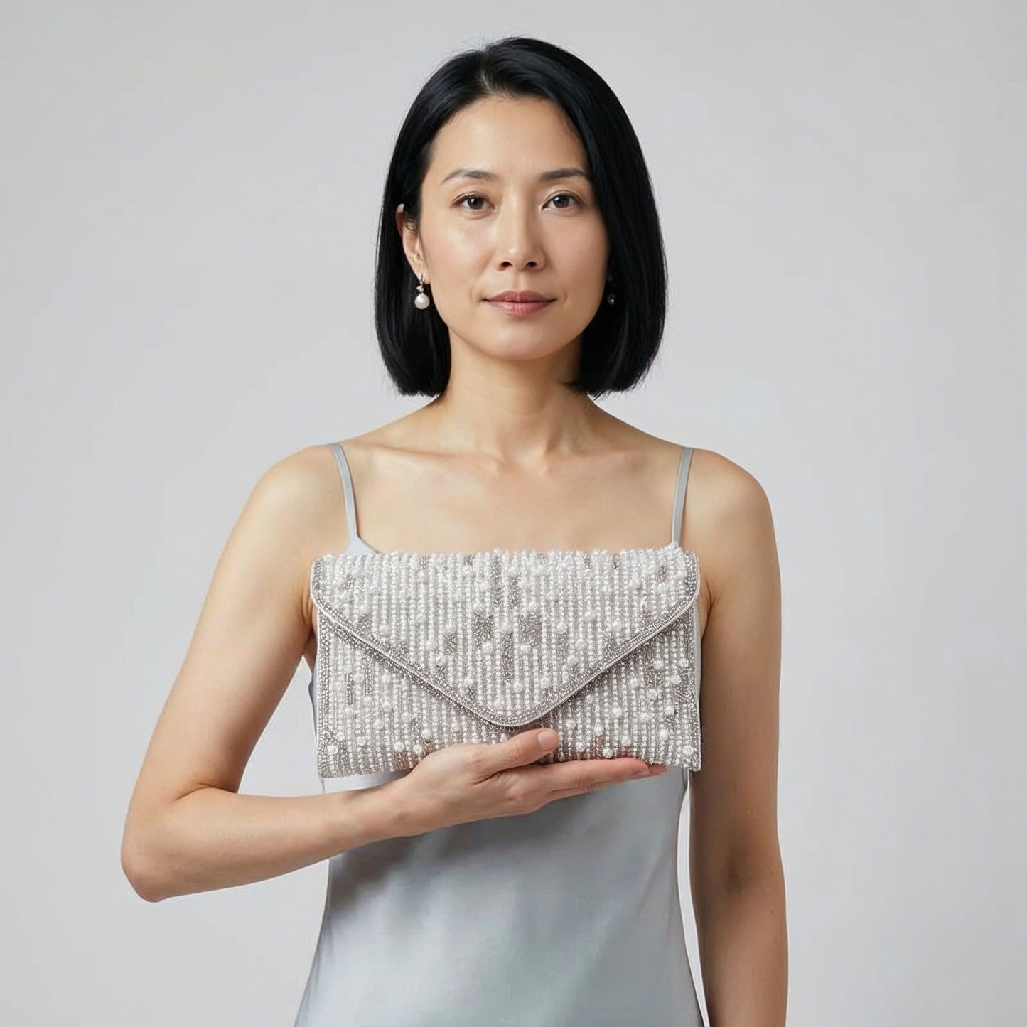 Model presenting the Silver Perlette Pearl & Crystal Envelope Clutch on her open palm, studio shot