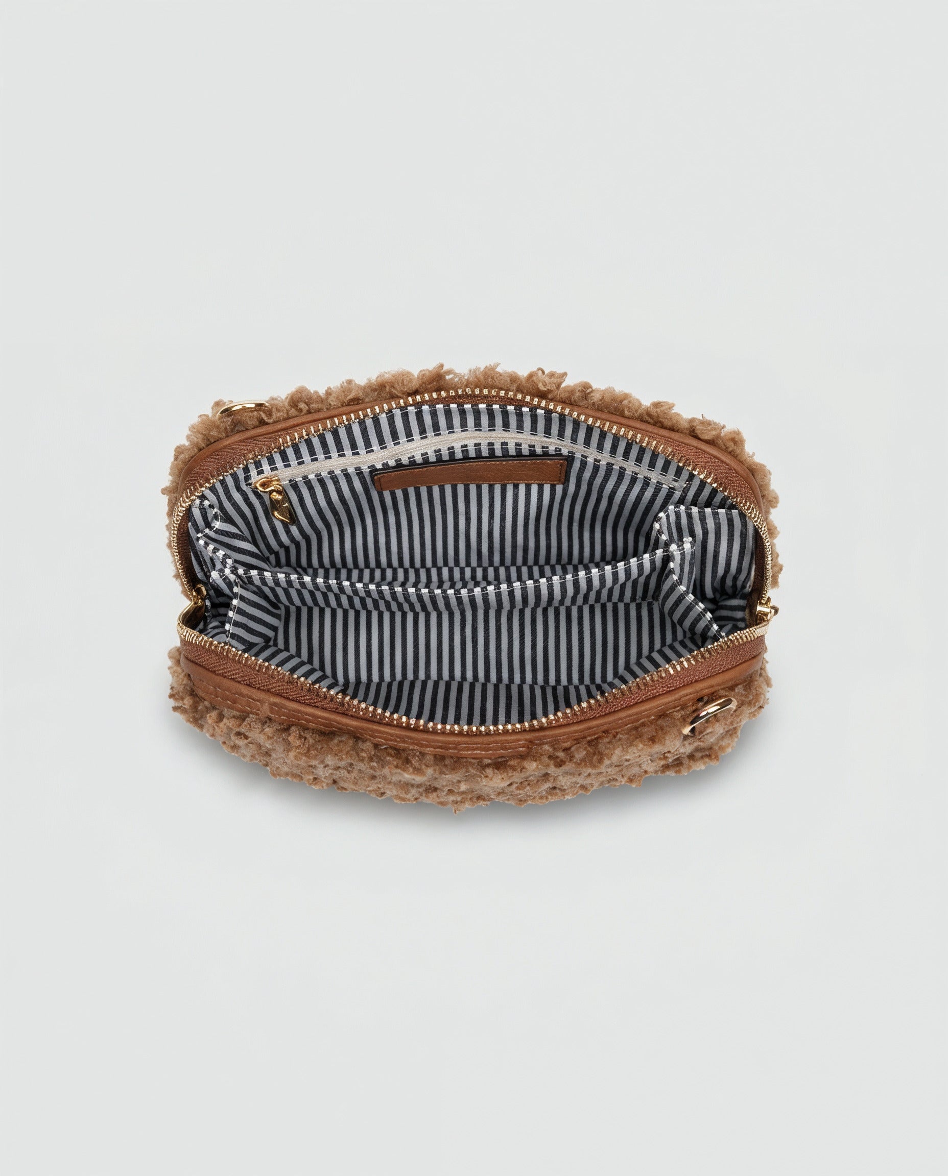 Zita faux shearling crossbody bag in tan shown open, revealing striped interior, light grey studio background