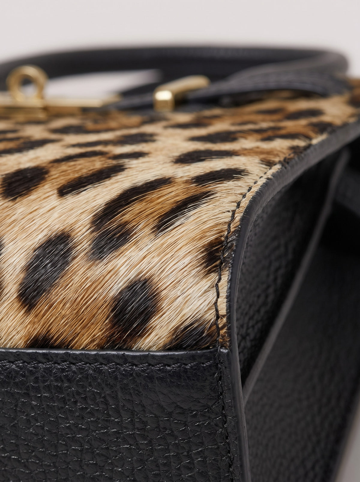 Extreme close-up of the Leonora real leopard-print calf hair bag, the hair panel stitched to the black Togo leather side seam