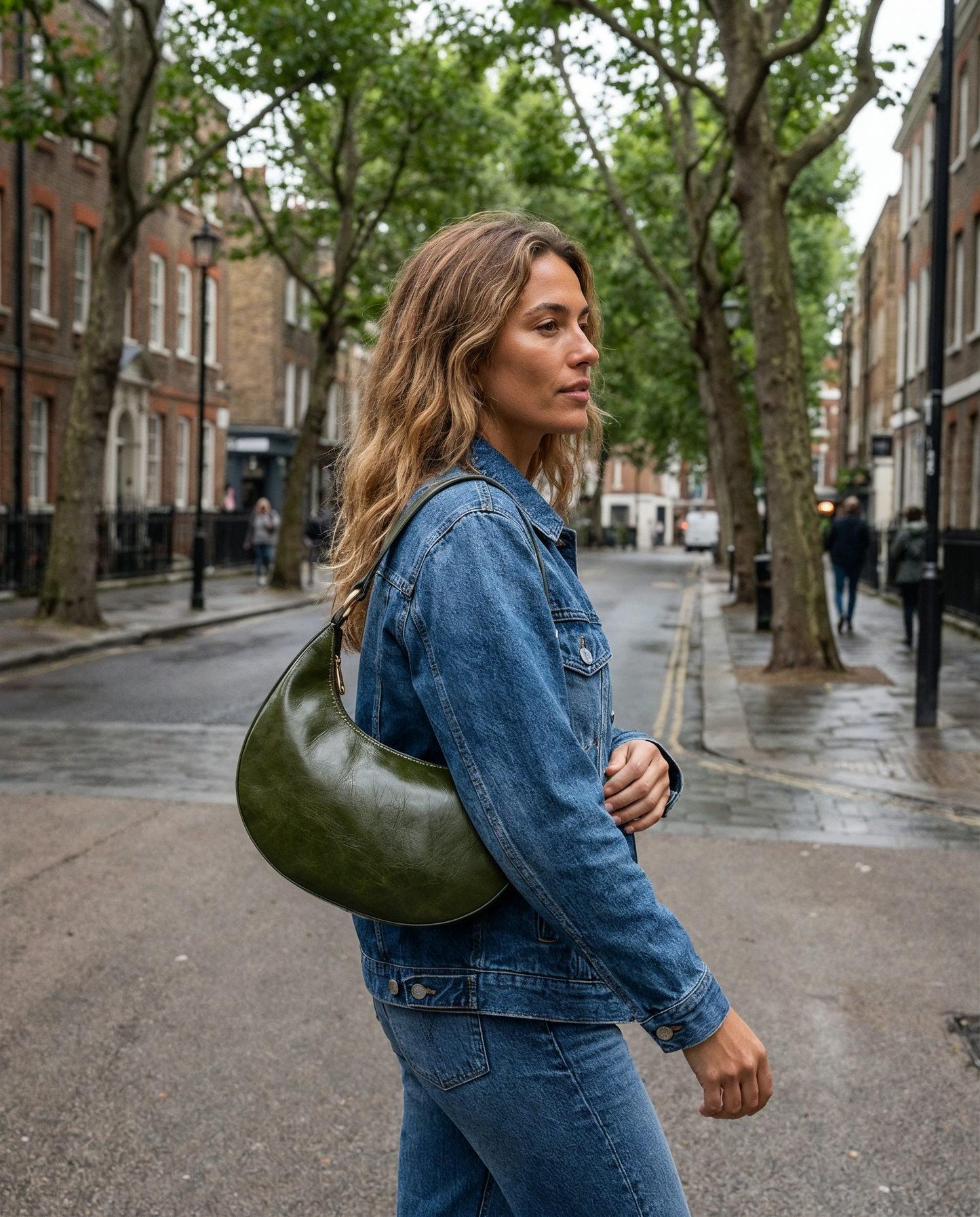 Woman wearing the Dark Olive Mezzaluna bag on her shoulder, walking on a city street