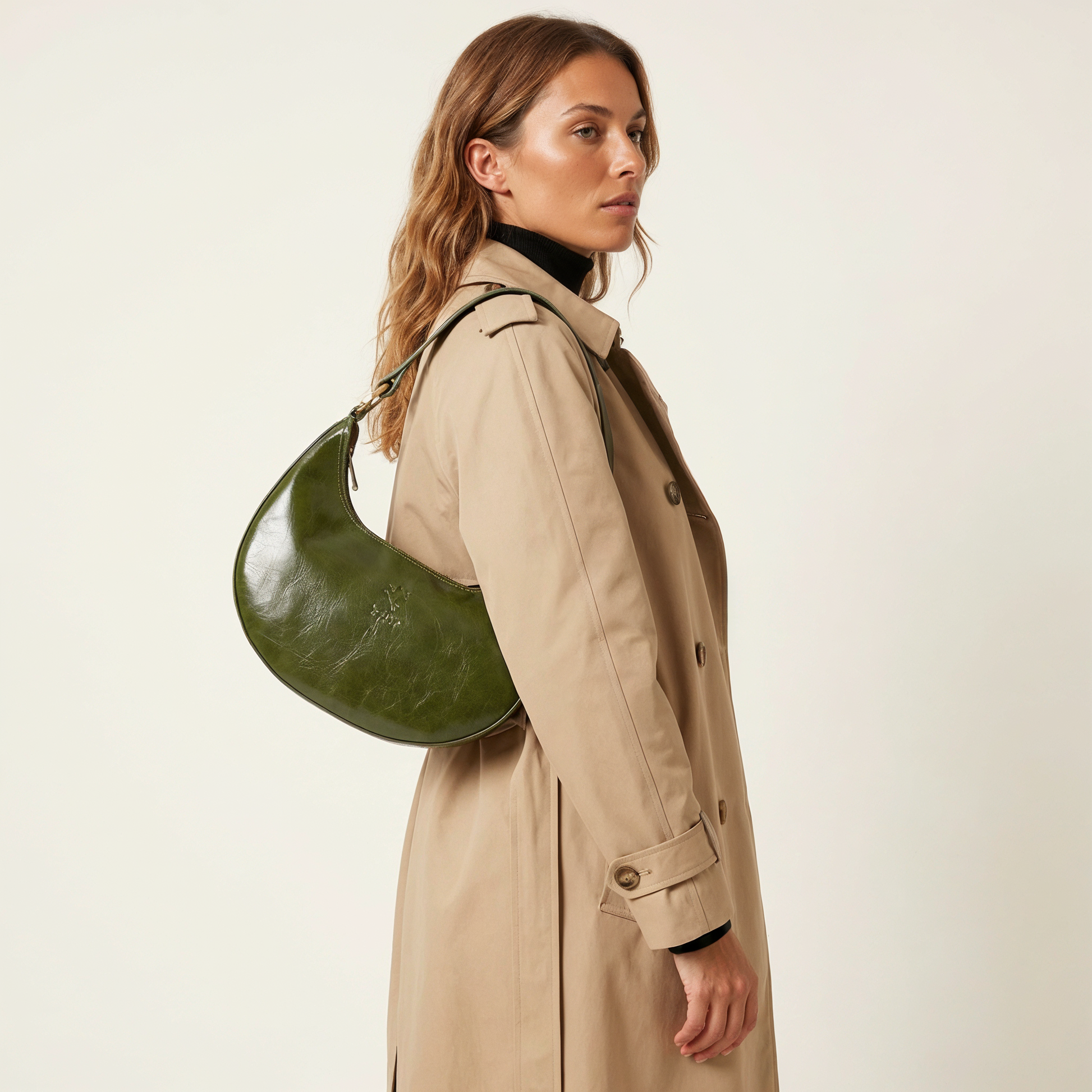 Woman wearing the Dark Olive Mezzaluna bag on her shoulder in a trench coat