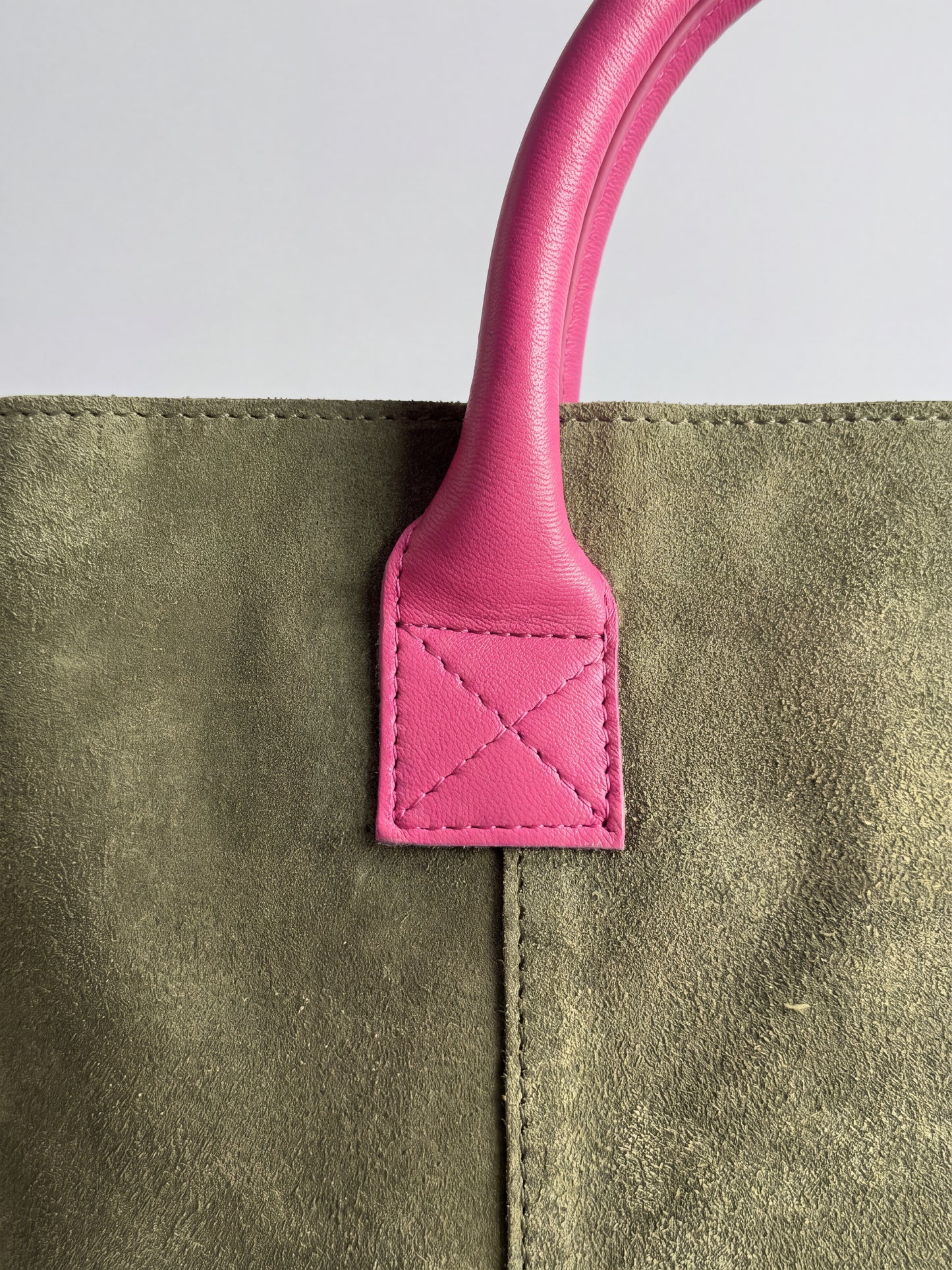 Milano Max Suede Bag in Olive by Clemés, macro detail of the fuchsia pink leather handle tab with cross stitching on olive suede
