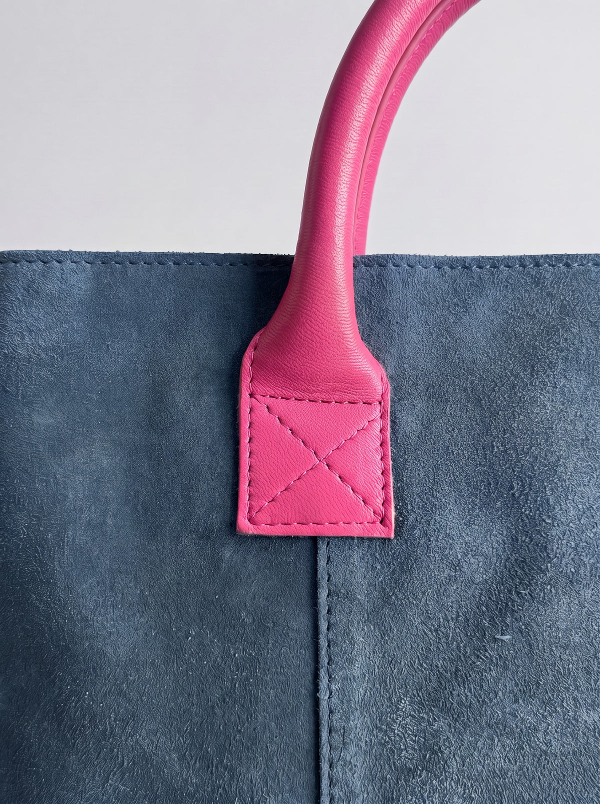 Milano Max Suede Bag in Blue by Clemés, macro detail of the fuchsia pink leather handle tab with cross stitching on blue suede