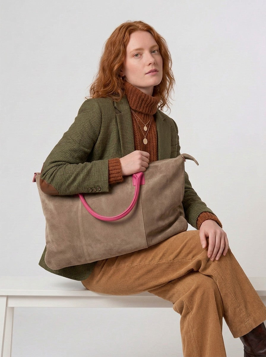 Model seated on a white bench carrying the Taupe Milano Max Suede Bag by Clemés on her shoulder, fuchsia pink handle