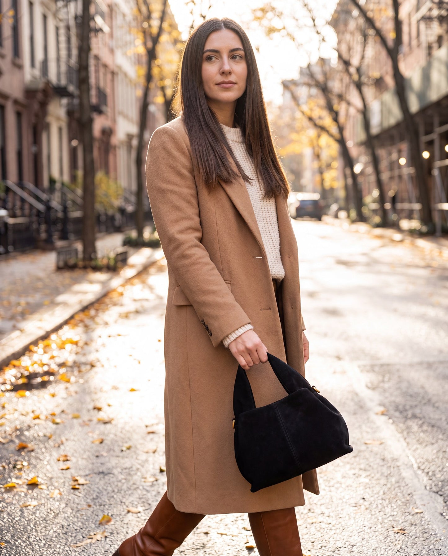 Woman carrying the Black Noemi Suede Handbag by its top handle on an autumn street strewn with fallen leaves