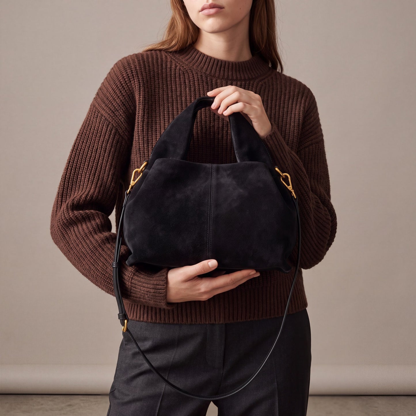 Model holding the Black Noemi Suede Handbag with both hands at waist height, studio shot