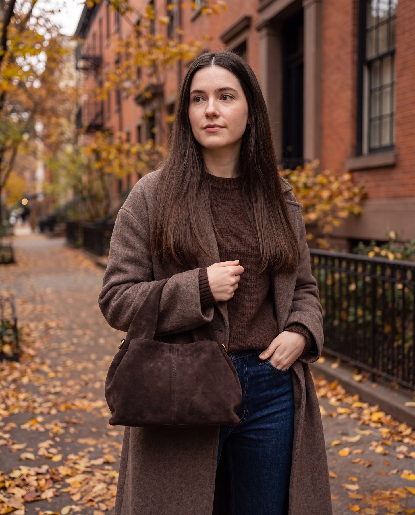 Woman carrying the Dark Brown Noemi Suede Handbag on an autumn street with golden leaves