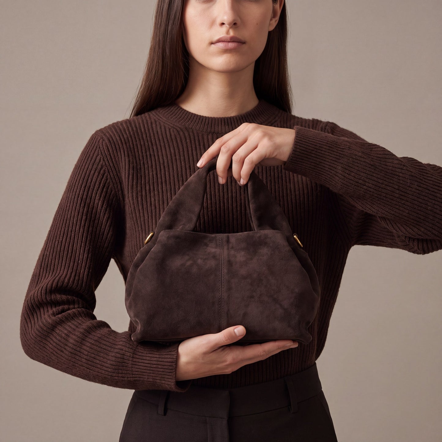 Model holding the Dark Brown Noemi Suede Handbag by its wide top handle, studio shot