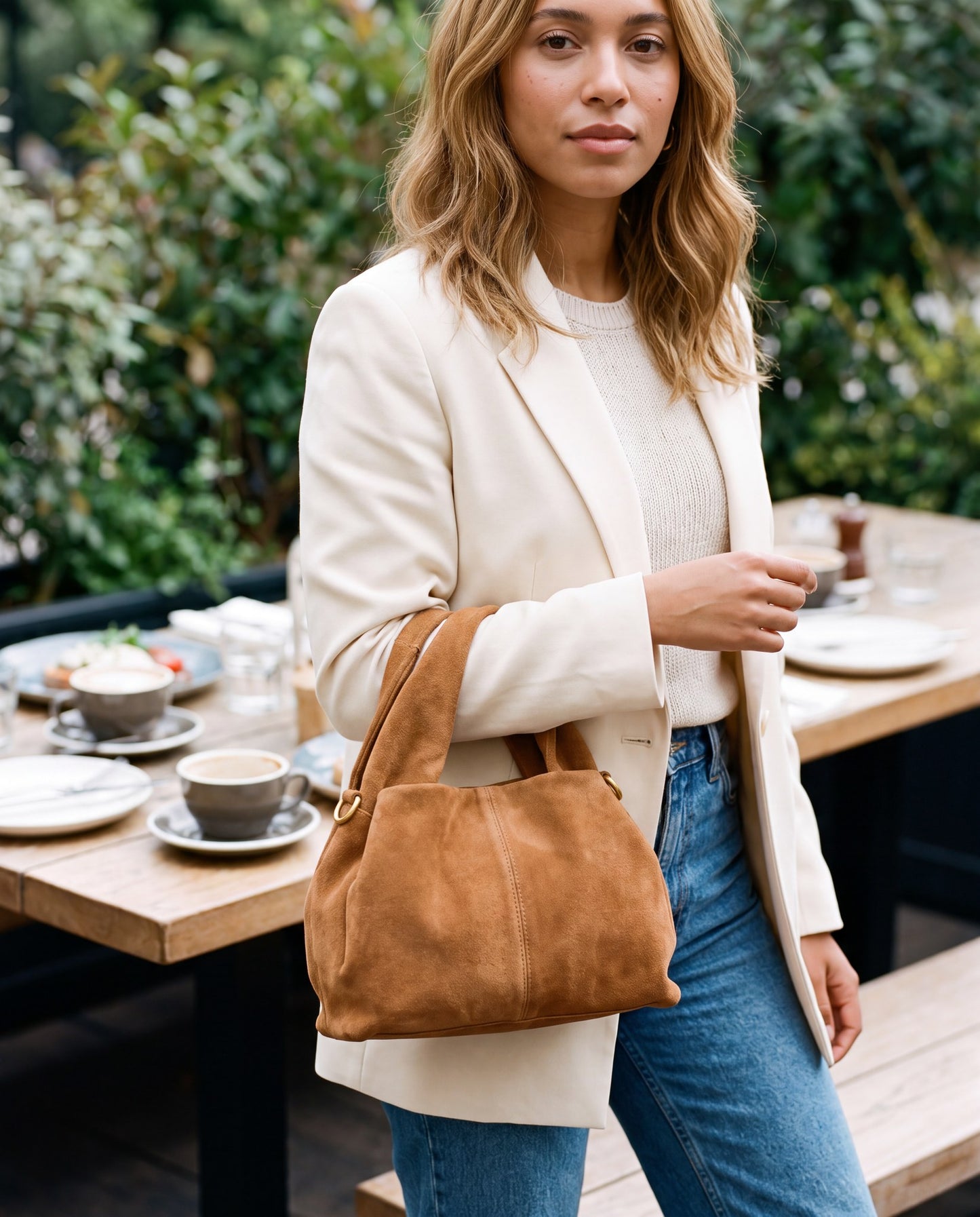 Woman leaving an outdoor brunch table with the Tan Noemi Suede Handbag on her arm