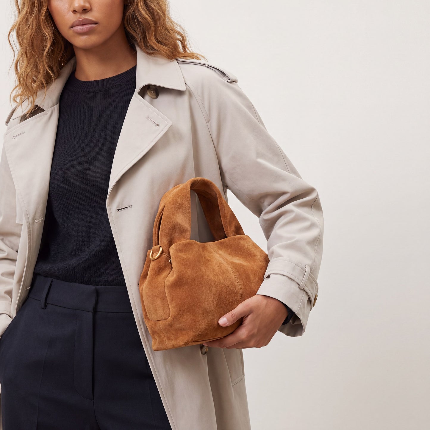 Model holding the Tan Noemi Suede Handbag in one hand at hip height, studio shot